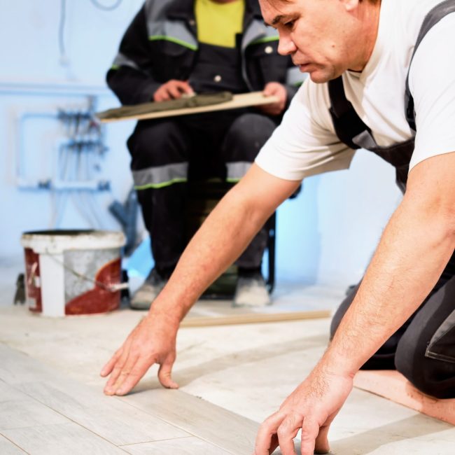 Installing ceramic floor tiles in construction site construction workers. Workers laying tiles on the floor with cement adhesive. Renovating the floor. Vertical frame Installing ceramic floor tiles in construction site construction workers. Workers laying tiles on the floor with cement adhesive. Renovating the floor. Vertical frame
